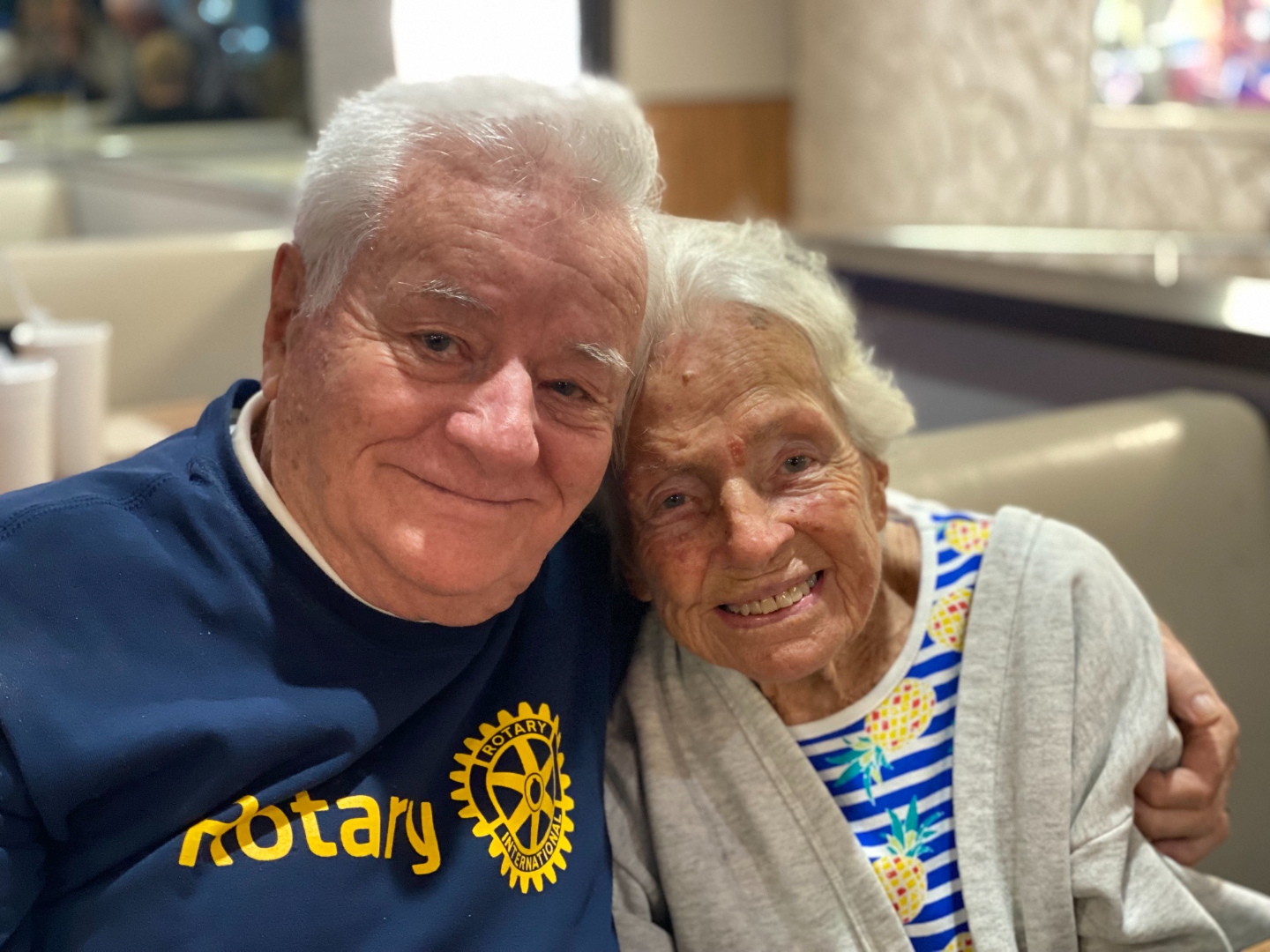 Portrait of Jerry Krauss in a Rotary sweatshirt with his arm around his wife Joan, both smiling warmly.